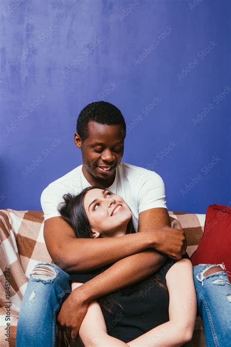 Young Happy Couple In Love Black Man And White Woman Cuddle And Caress On Couch At Home