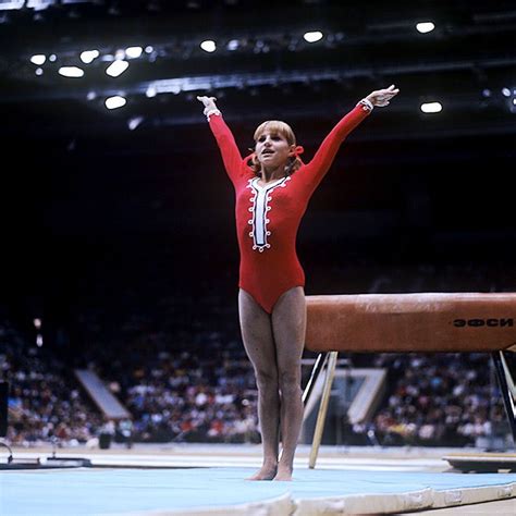 A Woman In A Red Leotard Standing On A Balance Beam With Her Arms Outstretched