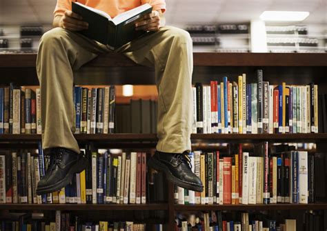 Man Reading Book And Sitting On Bookshelf In Library Jeet Banerjee