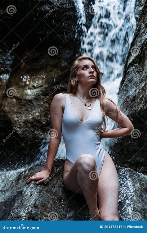 Vertical Shot Of A Woman In A Wet One Piece Swimsuit Sitting On A Rock
