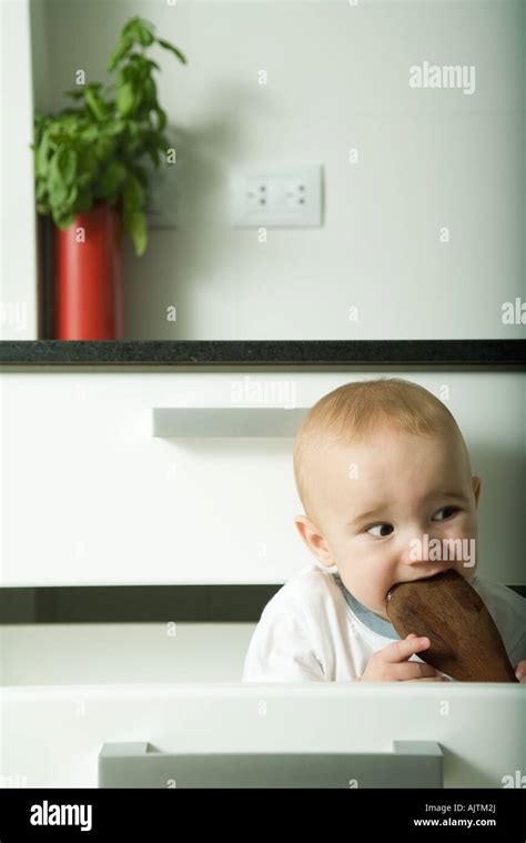 Baby In Drawer Biting On Wooden Spoon Making Funny Face Stock Photo