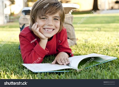 Very Cute 7 Year Old Boy Lying On The Grass Reading A Kids Book Stock