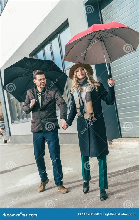 Stylish Young Couple In Autumn Outfit Holding Umbrellas Stock Photo