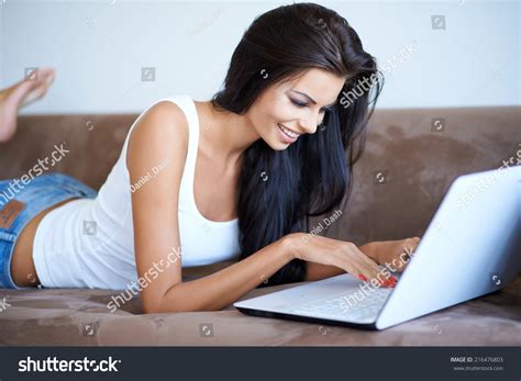Young Woman Lying On Her Stomach A Sofa Using A Laptop Computer To Surf The Internet With A