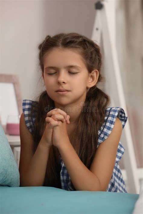Cute Little Girl With Hands Clasped Together Praying At Home Stock