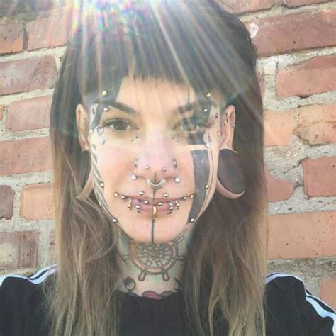 A Woman With Tattoos And Piercings On Her Face Standing In Front Of A Brick Wall