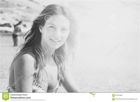 Beautiful Tanned Girl In A Bikini Sitting On A Rocky Beach Stock Image