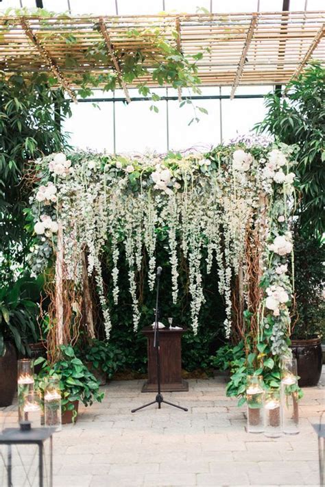 An Outdoor Ceremony Setup With White Flowers And Greenery On The Wall