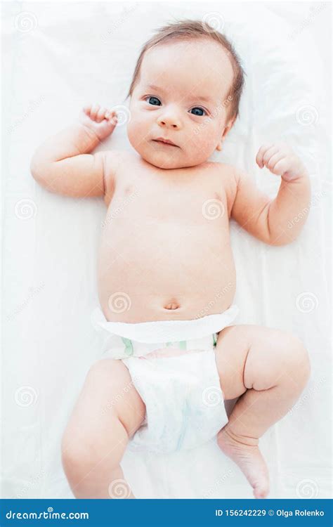 Funny Little Baby Wearing A Diaper Lying On A White Sheet Child After