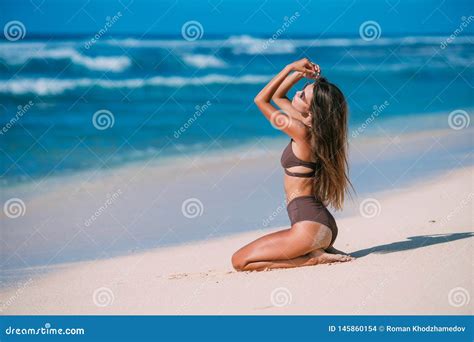 Tanned Model With Sunglasses In Brown Swimsuit Posing On White Sandy