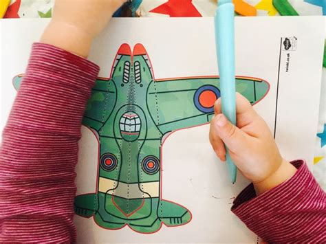 A Child Is Drawing On A Paper With A Blue Pencil And Some Colored Crayons