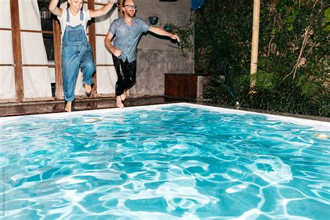Young Couple Wearing All Their Clothes Splashes Into Pool During