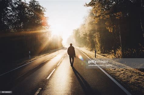 Rear View Of Man Walking On Road During Sunrise High Res