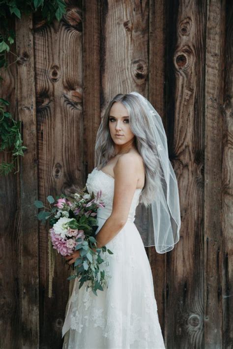 A Woman In A Wedding Dress Is Standing Near A Wooden Fence With Her
