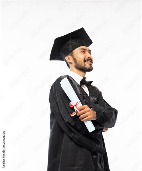 Confident Asian Male Graduate Wearing Toga And Holding A Roll Of
