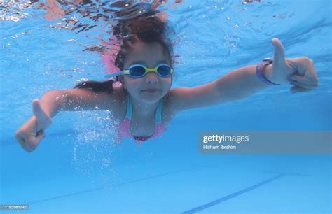 7 Years Old Girl Swimming Underwater In Swimming Pool Showing Thumbs Up