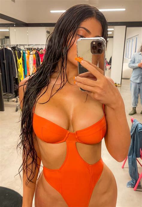 A Woman In An Orange Swimsuit Taking A Selfie With Her Cell Phone While Standing In A Clothing Store
