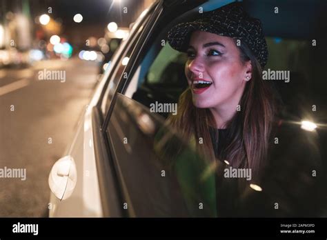 Woman Sitting On The Backseat Of A Car In The City At Night Looking Out Of The Car Window Stock