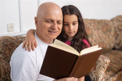 Happy Grandfather And Granddaughter Reading Book Together At Home