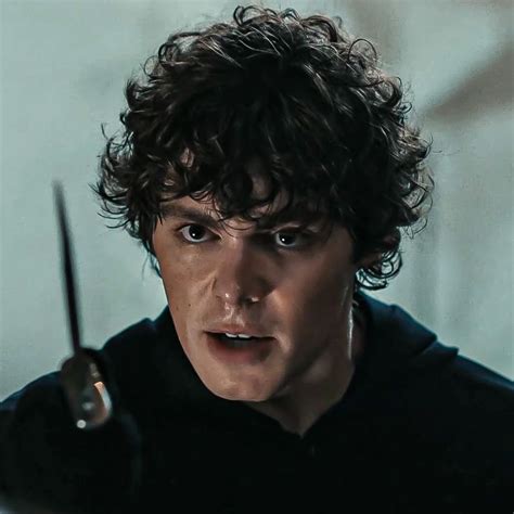 A Man With Curly Hair Holding Scissors In His Right Hand And Looking At