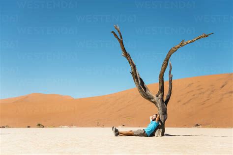 Namibia Namib Desert Man Resting At Dead Tree In Deadvlei Stock Photo