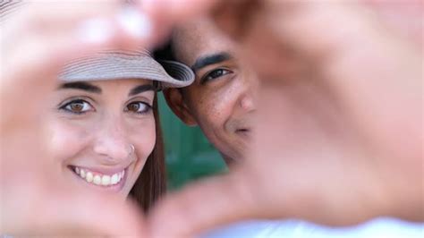 mixed race couple do heart sign with hands looking to camera love and relationship by