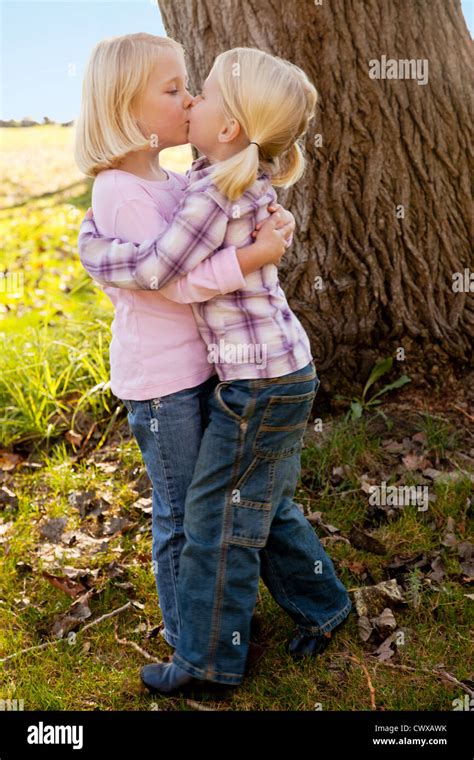 Twin Blond Girls Are Standing Beside Each Other In Front Of A Tree