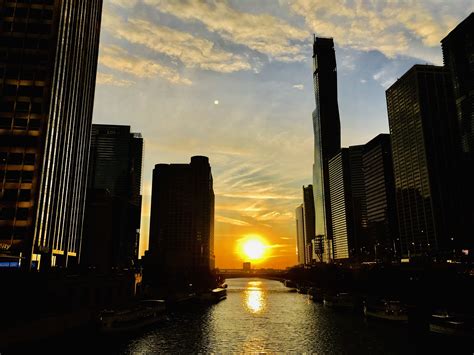 The Sun Is Setting Behind Some Tall Buildings On The Water In Front Of