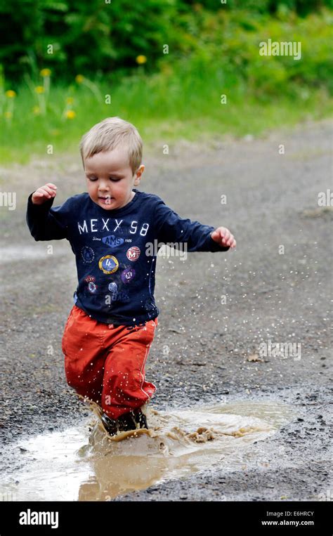 A Young Boy Getting Soaked Running Through A Puddle Stock Photo Alamy