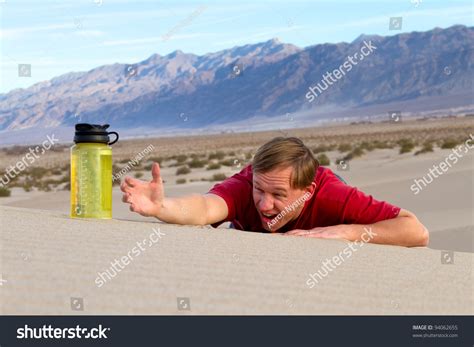 A Thirsty Man In The Desert Reaches For A Bottle Of Water Stock Photo