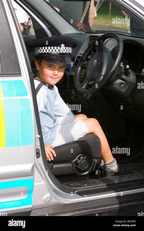 Small Boy Wearing A Police Hat Sitting In The Driving Seat Of A Police