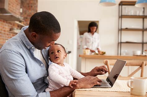 Father And Baby Daughter Use Laptop As Mother Prepares