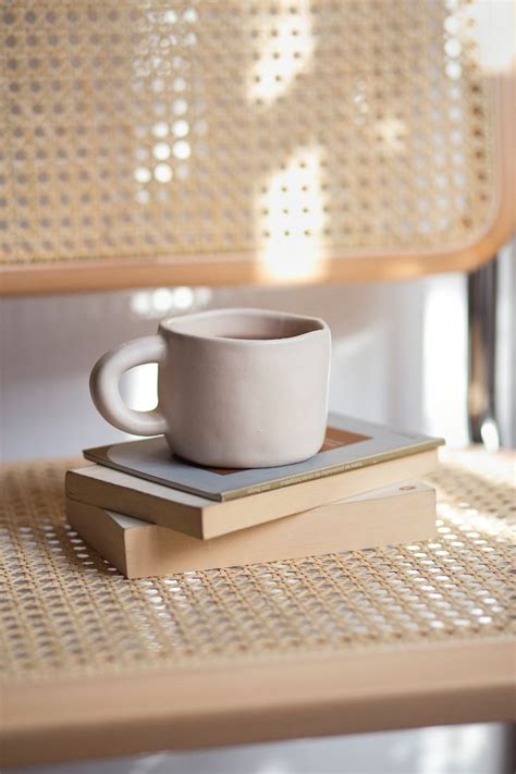 A White Cup Sitting On Top Of A Stack Of Books Next To A Wooden Bench