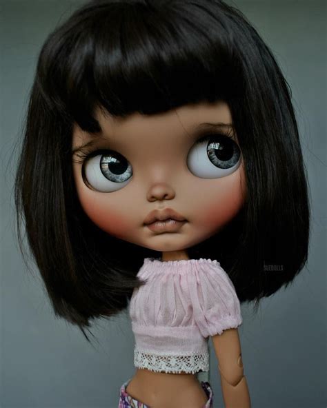A Close Up Of A Doll With Big Blue Eyes And Black Hair Wearing A Pink Dress