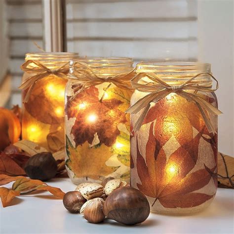 Three Mason Jars With Lights In Them Sitting On A Table Next To Leaves