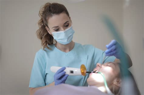 Young Female Dentist Treating Teeth Of Patient With Instruments In
