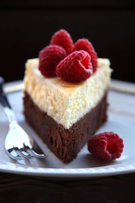 A piece of cheesecake with raspberries on top sits on a white plate