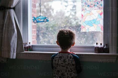 A Little Boy Looks Out A Window In His Bedroom Stock Photo