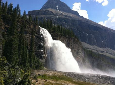 A Large Waterfall Is In The Middle Of Some Trees And Mountains With