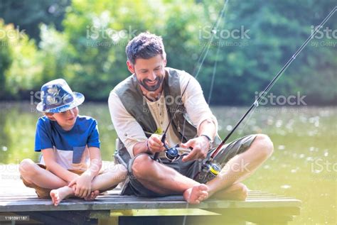 Padre E Hijo Pescando En Lake Mientras Están Sentados En El Muelle Foto