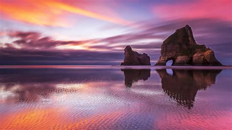 Rocks On Calm Body Of Water Under Black Yellow Clouds Blue Sky Horizon