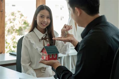 Real Estate Agent Holding House Key To His Client After Signing Contract Agreement In Office