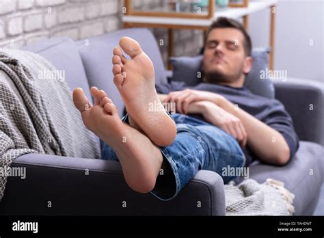 Close Up Of Man Relaxing On Sofa With His Legs Crossed In Home Stock