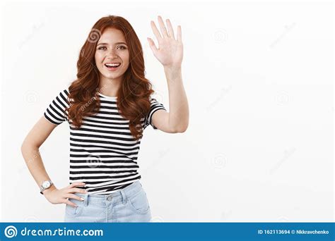 hello how you doing cheerful friendly cute redhead teenage girl in striped t shirt raising hand