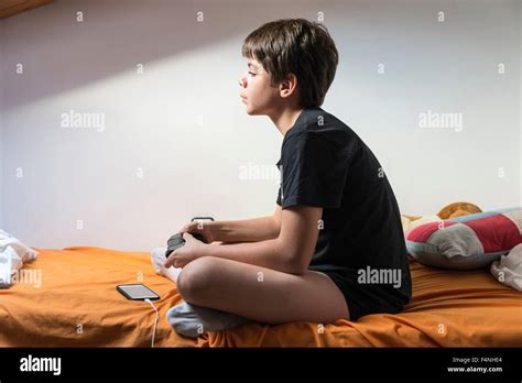 Young Boy Playing Video Games Sitting On The Bed In Her Room While