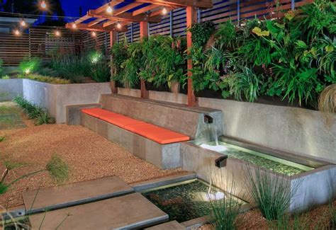 An Outdoor Garden With Water Feature And Seating Area At Night