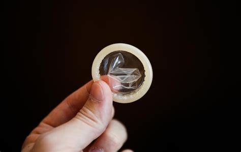 Рука держит презерватив с вич и обертками для безопасного секса на заднем плане пропаганда