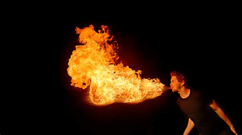 Male Fire Breather Blowing Fire Ball From Her Mouth Against Black