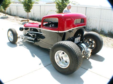 an old fashioned hot rod car is parked on the sidewalk in front of a fence