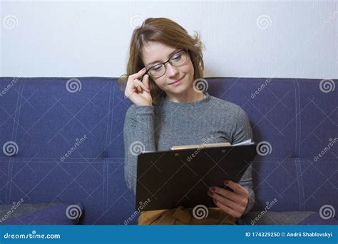 Young Pretty Woman In Glasses Sitting On A Sofa In The Office Reads